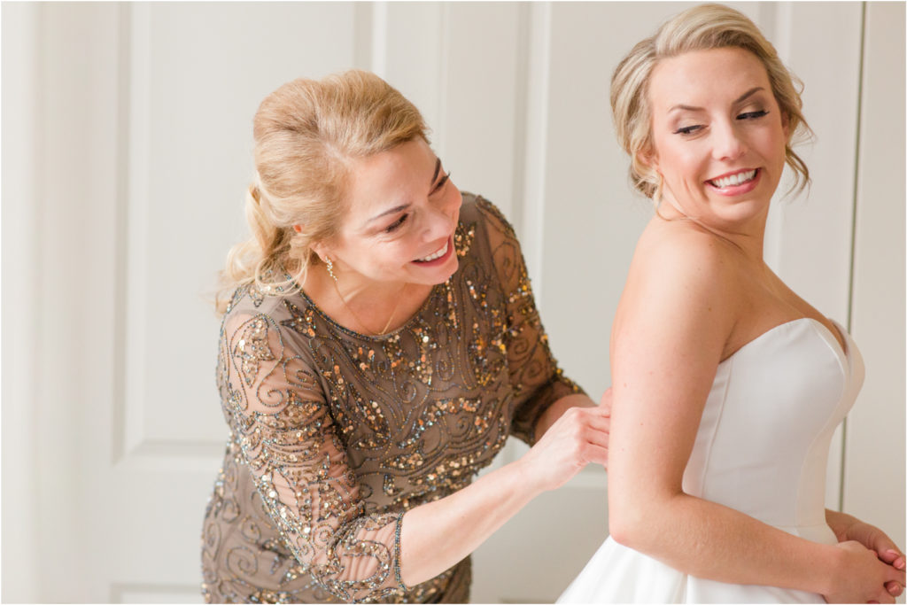 mom and daughter putting on wedding dress